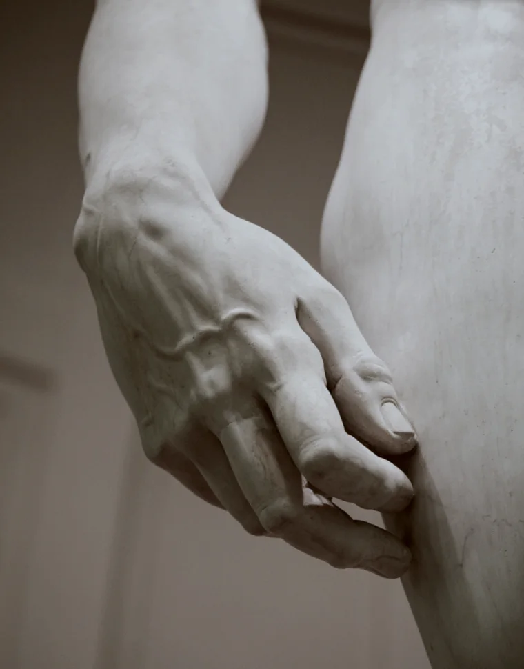 Detail of the left hand of Michelangelo’s David, veins swollen, resting against the thigh